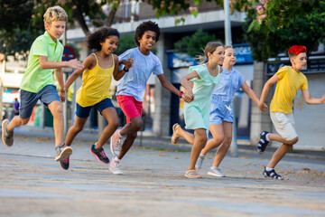 Fototapeta premium Happy tween friends having fun together on summer city street, running holding hands..