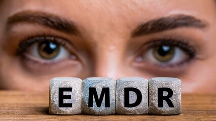 Eye Movement Desensitization and Reprocessing Psychotherapy Treatment concept. Letters EMDR written on grey cubes. Close up-view of woman's face with a focused look behind.