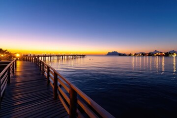 Obraz premium A splendid night view along a tranquil boardwalk, beautifully illuminated by soft lights, guiding guests toward serene waters and a vibrant evening sky.
