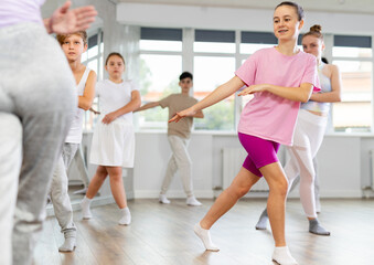 Female girl student repeats movements of unrecognizable teacher during group modern dance class. Hobbies, active pastime, additional extracurricular activities for children and teenagers