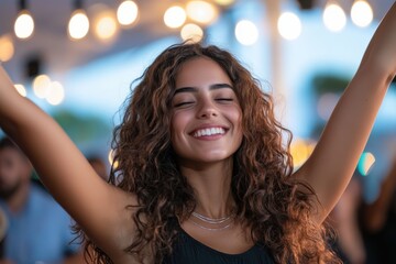 A young woman joyfully raises her arms in celebration, her beaming smile embodying the essence of happiness and enjoyment in a lively atmosphere filled with lights.