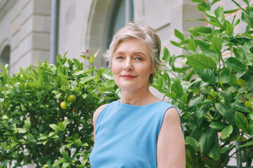 Outdoor summer portrait of mature woman with grey hair, posing with green foliage