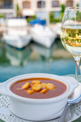 Homemade tasty fish or bisque soup with croutons served with glass of cold white wine and view on yacht boats and houses of Port Grimaud, French Riviera, France. Food of Provence
