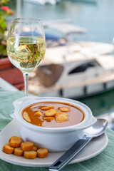 Homemade tasty fish or bisque soup with croutons served with glass of cold white wine and view on yacht boats and houses of Port Grimaud, French Riviera, France. Food of Provence