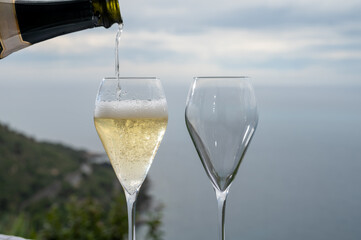 Pouring of cold sparkling wine, cava or champagne in two glasses on table with sea water view