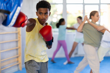 Trainer and boy in boxing gloves train boxing punches in the studio..