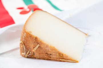 Piece of tasty Basque Brebis Fume smoked sheep cheese produced in south-western France, Northern Basque Country and towel with Basque symbol and colours