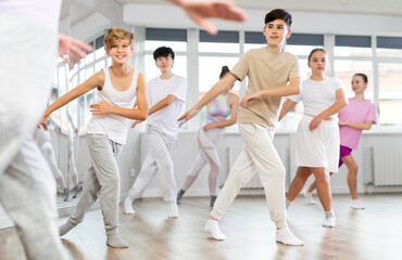 Fototapeta premium Teenage boy rehearse hip hop dance repeats movements of unrecognizable instructor performance with peers. Preparing for performance of choreographic team, practicing skills, repeating exercises