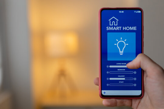 Hand interacting with smartphone app, adjusting lighting settings for different rooms in a smart home environment. IOT concept