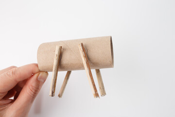 Hands holding DIY craft made from cardboard tube and small sticks. Simple handmade project resembling rocking horse. Creative upcycling idea using everyday materials for crafting, learning, and fun,