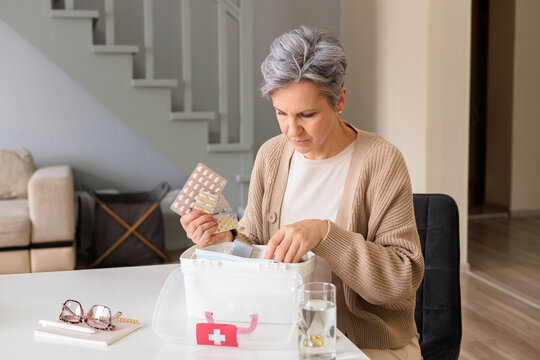 Beautiful aged woman pensioner with gray hair checking medicines at domestic first aid kit.