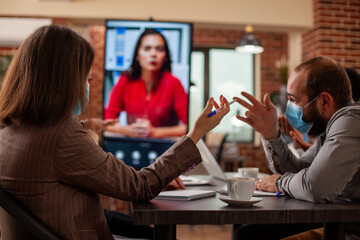 Male and female coworkers discuss marketing strategies while viewing a female client on digital monitor during team meeting. Startup team attending videocall on screen with the remote businesswoman.