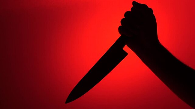 Silhouette of hand holding knife on red background representing violence