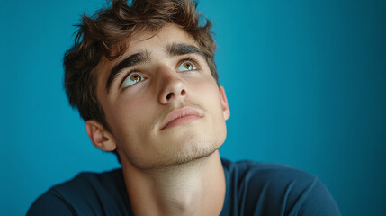 A young man, looking up with a curious and thoughtful face expression. thinking of an idea to solve a problem, clever man, studio shot, isolated on a blue background, wondering, guessing.