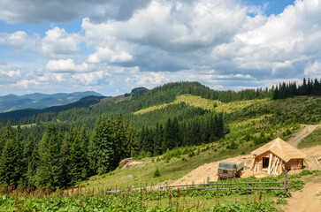 Verdant countryside featuring small wooden cabin with logs beside it, surrounded by green hills and...
