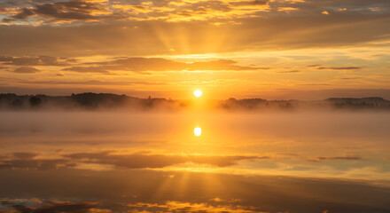 Fototapeta premium Golden clouds reflecting the first rays of sunrise over a tranquil, misty lake