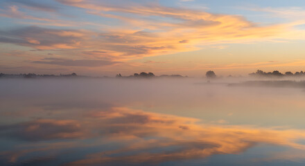Obraz premium Golden clouds reflecting the first rays of sunrise over a tranquil, misty lake