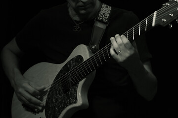 Fototapeta premium Black and white close-up of a guitarist's hands playing an electric hybrid guitar on stage.