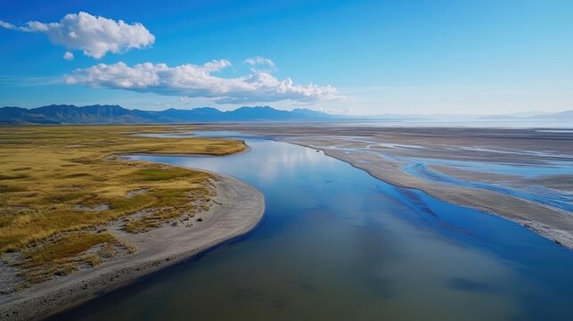 Panoramic view of a river meandering through marshlands towards a distant mountain range under a clear blue sky