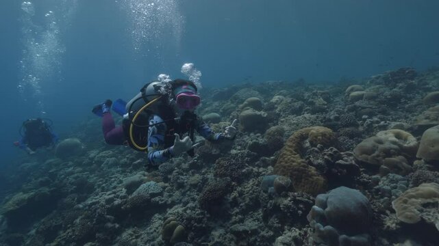 scuba divers ascending surface going back to boat underwater with sun beams and rays ocean scenery. Two women divera swim past camera above coral reef. Extrime sport activity, underwater tourism.