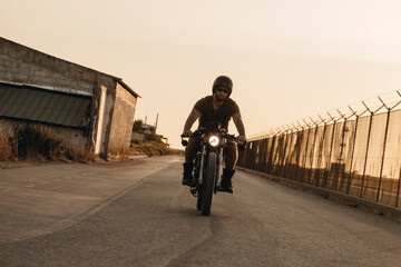 Biker riding custom motorcycle on empty road at sunset