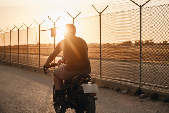 Biker riding motorcycle along airport perimeter fence at sunset