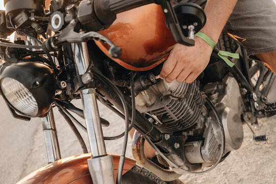 Mechanic fixing engine of vintage orange motorcycle outdoors