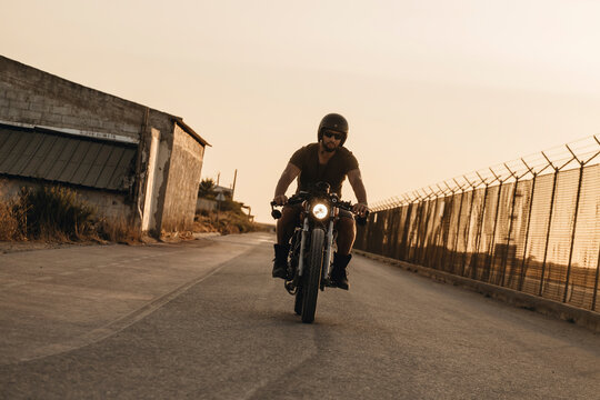 Biker riding custom motorcycle on empty road at sunset