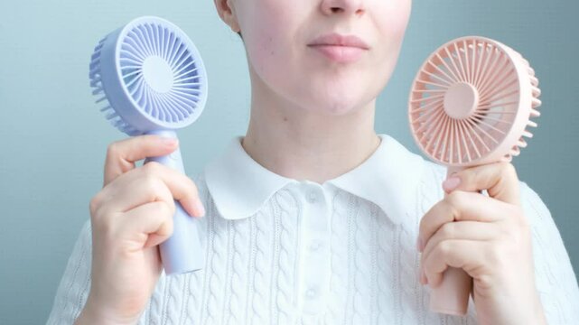 Young woman holding two mini fans on a gray background close-up, front view.