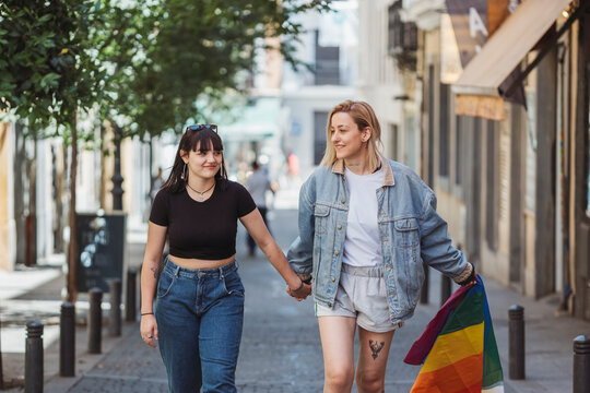 Lesbian couple holding hands and lgbt flag walking down the street
