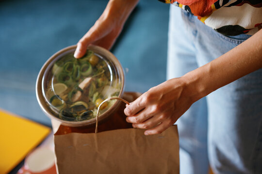 Cropped woman taking bowl with salad from package at blurred home