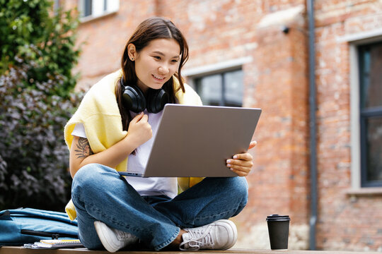 Pretty young smiling asian woman student or worker watching laptop