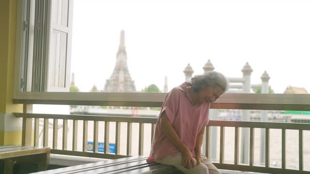 Travel and health insurance concept. Asian elderly woman get injury knee pain or leg cramp during travel in the city. Senior woman tourist travel Buddhist temple in Thailand on summer holiday vacation