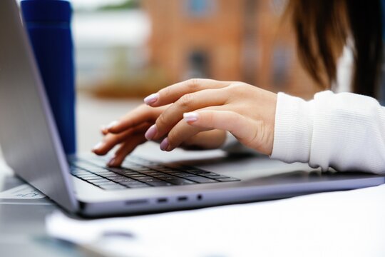 Partial of businesswoman typing laptop computer at table outdoors