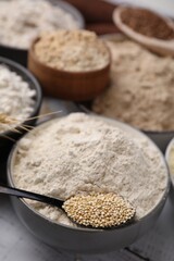 Bowls with different types of flour and ingredients on white wooden table, closeup