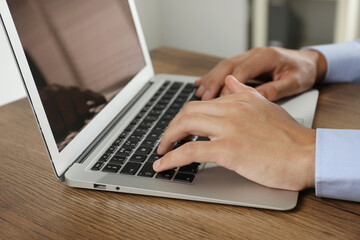 Businessman using laptop at wooden table, closeup. Modern technology