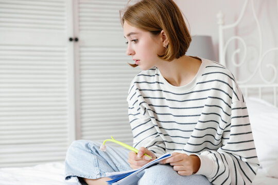 Female school student looking away during writing in notebook at home