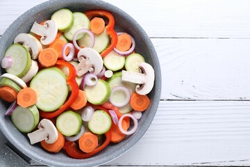 Frying pan with mix of fresh vegetables and mushrooms on white wooden table, top view. Space for text