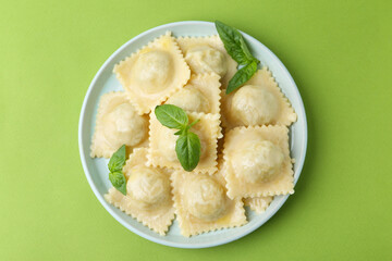 Delicious ravioli with cheese and basil on green background, top view