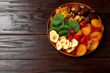 Mix of different dried fruits in bowl on wooden table, top view. Space for text