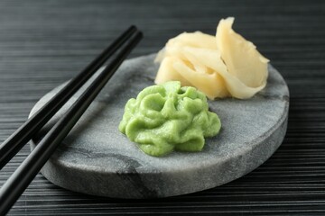 Marble board with hot wasabi paste, ginger and chopsticks on black textured table, closeup
