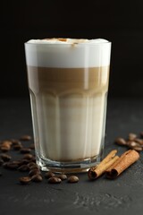Tasty latte macchiato in glass, coffee beans and cinnamon on black table, closeup