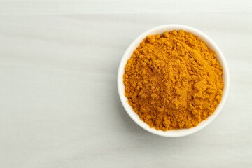 Turmeric powder in bowl on white table, top view. Space for text