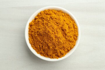 Turmeric powder in bowl on white table. Top view