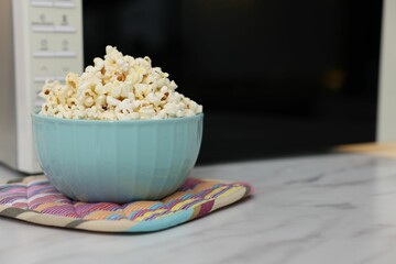 Tasty popcorn in bowl near microwave oven on light marble table, closeup. Space for text