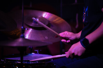 Drummer playing jazz with drumsticks, focus on hands and cymbals.