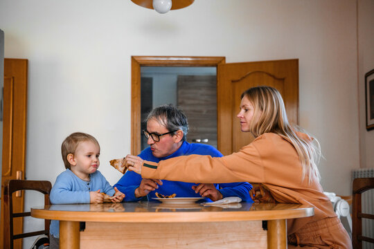 Mother holding out a slice of pizza to her son