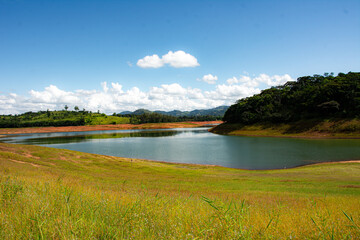 A scenic view of the Graminha reservoir in Caconde, São Paulo, showcasing clear blue water and surrounding lush green hills under a bright sky