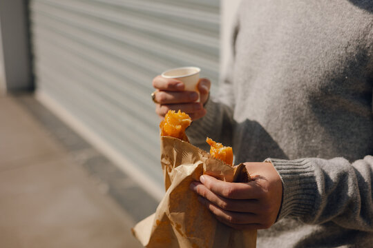 A male enjoying a pastry while holding a cop of coffee 