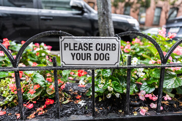 Please curb your dog sign hanging on a fence in New York City